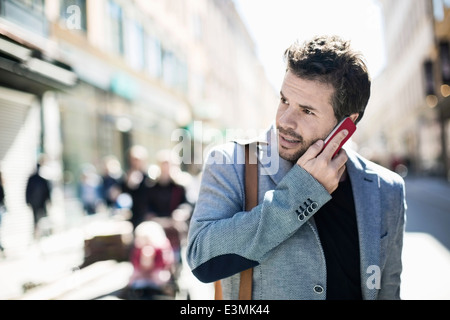 Mid adult businessman answering smart phone on city street Stock Photo