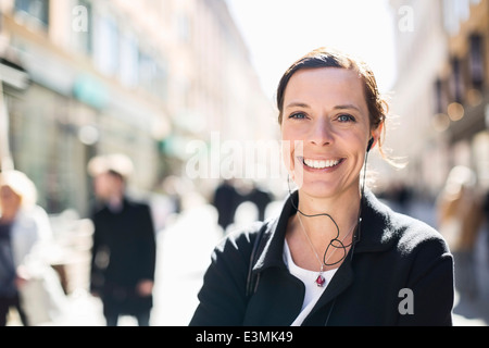 Portrait of smiling mature businesswoman listening to music on city street Stock Photo