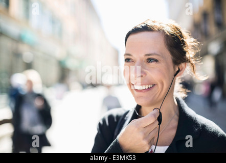 Smiling mature businesswoman talking through headphones on city street Stock Photo