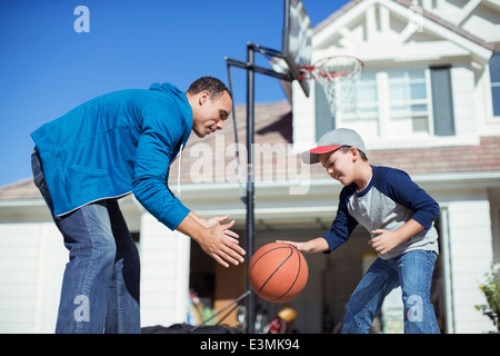 Father and son playing basketball in sunny driveway