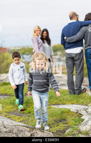 Children walking on rock with homosexual couple in background Stock Photo