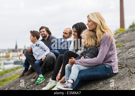 Homosexual families relaxing on rock at lakeshore Stock Photo