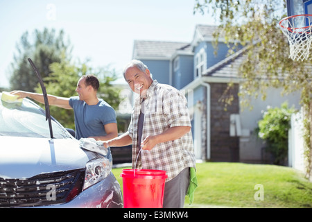 Portrait of smiling father and son washing car in driveway Stock Photo