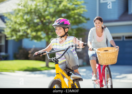 Mother and daughter riding bicycles in sunny street Stock Photo