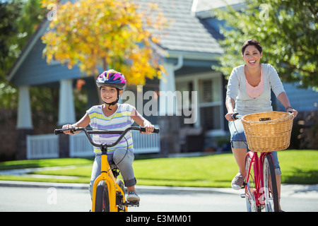 Mother and daughter riding bicycles in sunny street Stock Photo