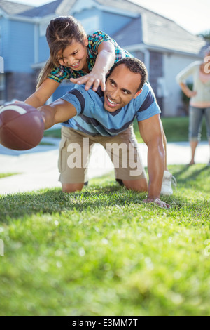 Father and daughter playing football in grass Stock Photo