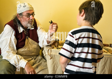 A lIving history re-enactor portraying a surgeon barber of English Civil war showing a small boy period medical equipment Stock Photo