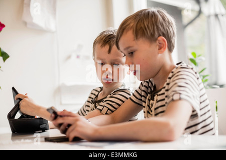 Brothers using mobile phone and digital tablet at table Stock Photo