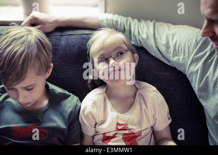 Girl with down syndrome looking at father by brother on sofa Stock Photo