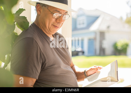 Man reading book on sunny patio Stock Photo