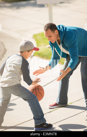 Father and son playing basketball in sunny driveway