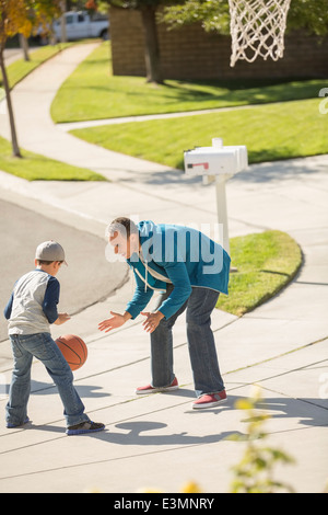 Father and son playing basketball in sunny driveway Stock Photo