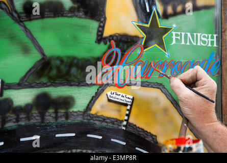 Skipton to Harrogate; Yorkshire Dales National Park, UK.  Eddie Ralph, local artist, completing his painting Window Art as Yorkshire prepares for Le Tour de France, The cycle artwork route is decorated with yellow Bikes and Banners as businesses gear up for the world's greatest cycle race which will start in the county on 5th & 6th July 2014 bringing millions of fans to the Yorkshire roadside to cheer on the champions of the sport.  It will be the first time Le Tour has visited the north of England having previously only made visits to the south coast and the capital. Stock Photo