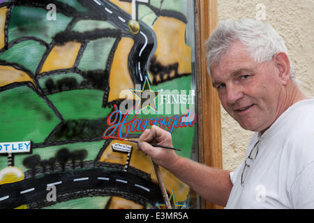 Skipton to Harrogate; Yorkshire Dales National Park, UK.  Eddie Ralph, local artist, completing his painting Window Art as Yorkshire prepares for Le Tour de France, The cycle artwork route is decorated with yellow Bikes and Banners as businesses gear up for the world's greatest cycle race which will start in the county on 5th & 6th July 2014 bringing millions of fans to the Yorkshire roadside to cheer on the champions of the sport.  It will be the first time Le Tour has visited the north of England having previously only made visits to the south coast and the capital. Stock Photo