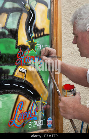 Window artist using mahlstick, or maulstick in Skipton  Yorkshire Dales National Park, UK.  Eddie Ralph, local artist, completing his painting as Yorkshire prepares for Le Tour de France, The cycle artwork route is decorated with yellow Bikes and Banners as businesses gear up for the world's greatest cycle race which will start in the county on 5th & 6th July 2014 bringing millions of fans to the Yorkshire roadside to cheer on the champions of the sport.  It will be the first time Le Tour has visited the north of England having previously only made visits to the south coast and the capital. Stock Photo