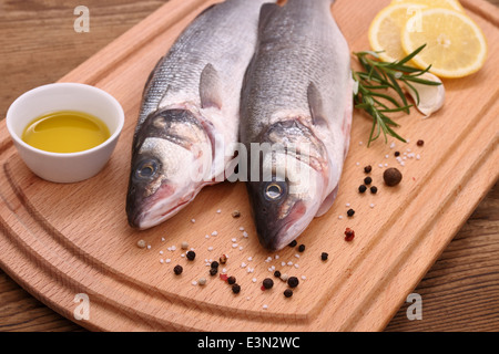 Two fresh sea bass fish on cutting board, ingredients, close up