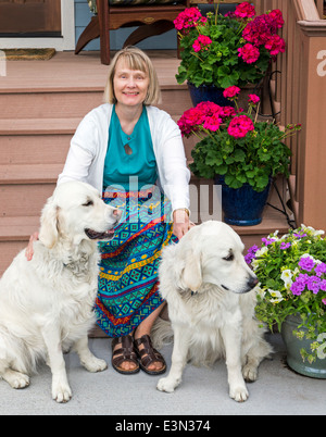 Woman posing for photograph on front porch with two platinum colored Golden Retriever dogs Stock Photo