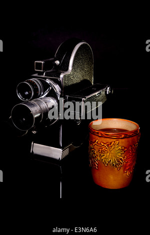 Vintage 16mm film camera and cup of coffee isolated over black Stock Photo