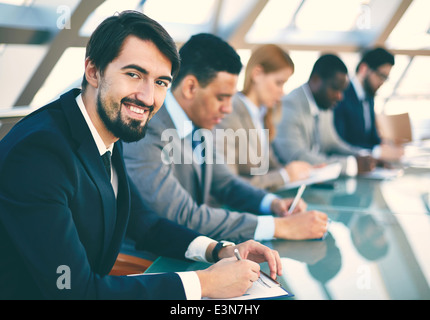 Row of business people listening to presentation at seminar with smiling young man on foreground Stock Photo