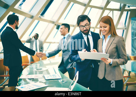 Two business people discussing data or planning work on background of their colleagues handshaking Stock Photo