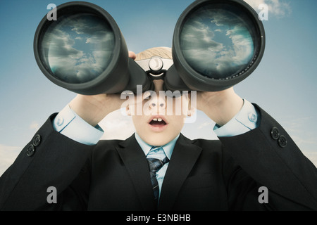 Boy dressed as businessman looking through binoculars against sky Stock Photo