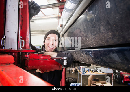 Portrait of confident male auto mechanic leaning on hoist in repair shop Stock Photo