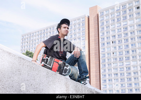 Thoughtful young man with skateboard sitting against building Stock Photo