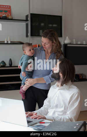 Father looking at woman and baby girl while using laptop Stock Photo