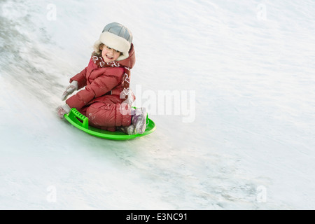 Full length of happy girl tobogganing in snow Stock Photo