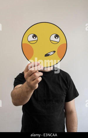Man holding a shy emoticon face in front of his face Stock Photo
