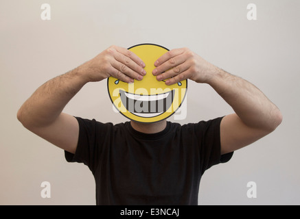 Man holding with hands covering the eyes of a happy emoticon face Stock Photo