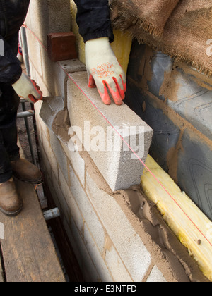 self building house, bricklayer laying concrete block wall with 100mm insulation Stock Photo