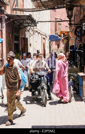 Lots of people on various modes of transport going along a narrow street in the Medina, Marrakech, Morocco Stock Photo