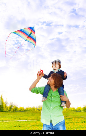 Father holds kid on shoulders with flying kite Stock Photo