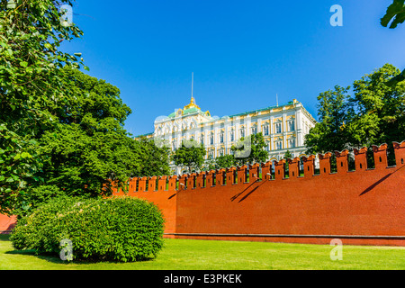 Grand Kremlin Palace behind the red Kremlin wall against clear blue sky and amidst green grass and trees Stock Photo