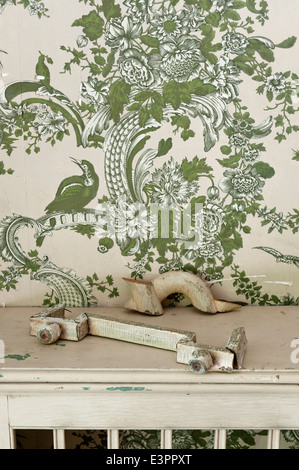 Piece of broken architectural salvage on ledge with patterned wallpaper behind Stock Photo