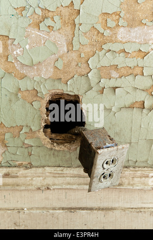 Old plug socket hanging out of hole in wall with cracked wall paint