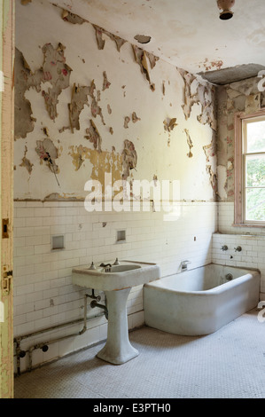 Old bathroom with torn peeling wallpaper, white wall tiling and honeycomb floor tiles Stock Photo