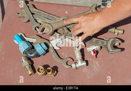 Many rusty wrenches and valves with reached out hand of plumber on light brown background. Stock Photo