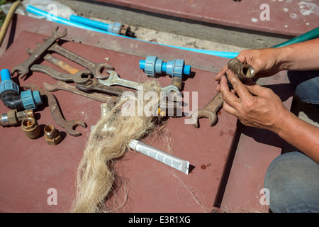 Hands of plumber that is checking the wye on the brown background with many rusty wrenches and valves. Stock Photo
