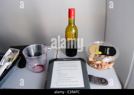 A half drunk bottle of red wine, a bowl of nuts and a Kindle on a seat table on board an airplane Stock Photo