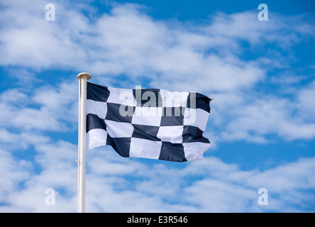 A checkered  race finish flag blowing in the wind against a blue and cloudy sky