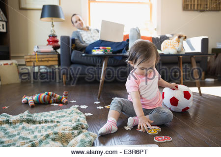 Father with laptop watching baby daughter play Father with laptop watching baby daughter play