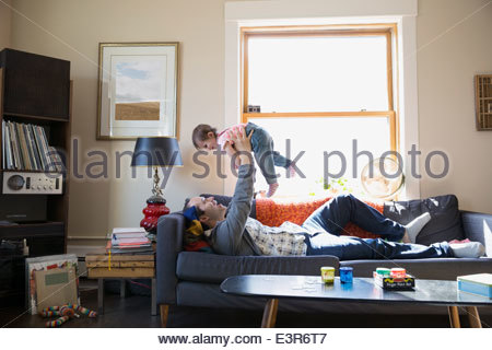 Father lifting baby daughter overhead on sofa