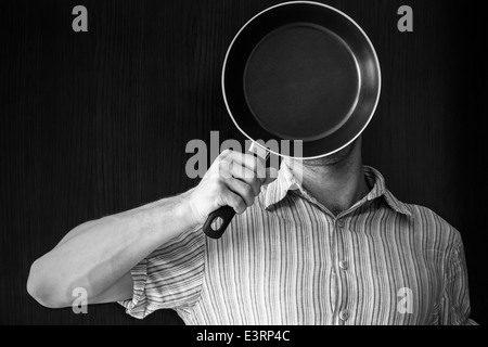 Young man monochrome portrait behind black frying pan Stock Photo