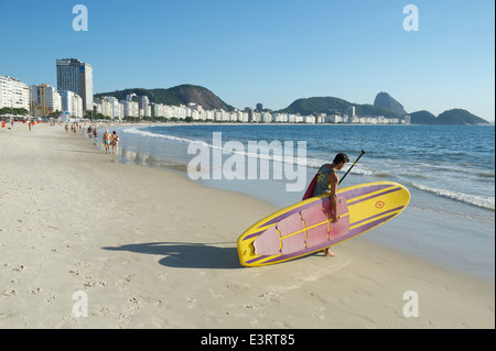 RIO DE JANEIRO, BRAZIL - JANUARY 31, 2014: Brazilian man carries a stand up paddle longboard surfboard into the water Copacabana Stock Photo