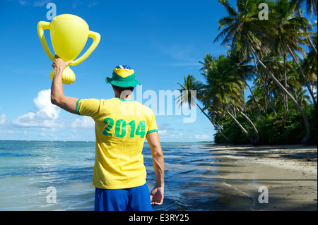 Brazilian football player in 2014 shirt Brazil colors holding trophy up on remote beach in Nordeste Bahia Stock Photo