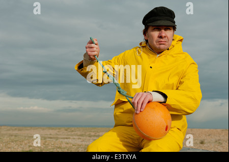 Sea fisherman in yellow waterproof overalls, standing by his fishing boat  and looking out to sea Stock Photo - Alamy