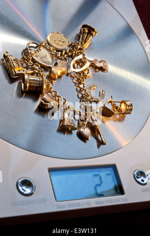 GOLD SCRAP VALUE SALE SELL SELLING WEIGHING WEIGHT old gold charm charms bracelet on weighing machine displaying 27 grams in weight Stock Photo