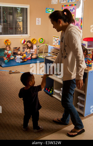 An Asian mother and her toddler son attend a 'Learning Link' interactive classroom in Tustin, CA. Using specially designed activities, the class teaches parents how to engage their children in meaningful play. Note play group in background. Stock Photo
